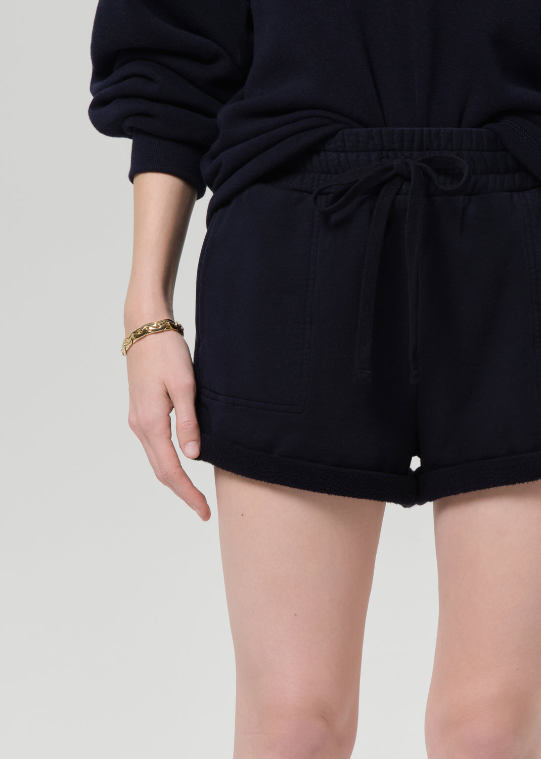 Person wearing a navy sweatshirt and shorts on a grey background