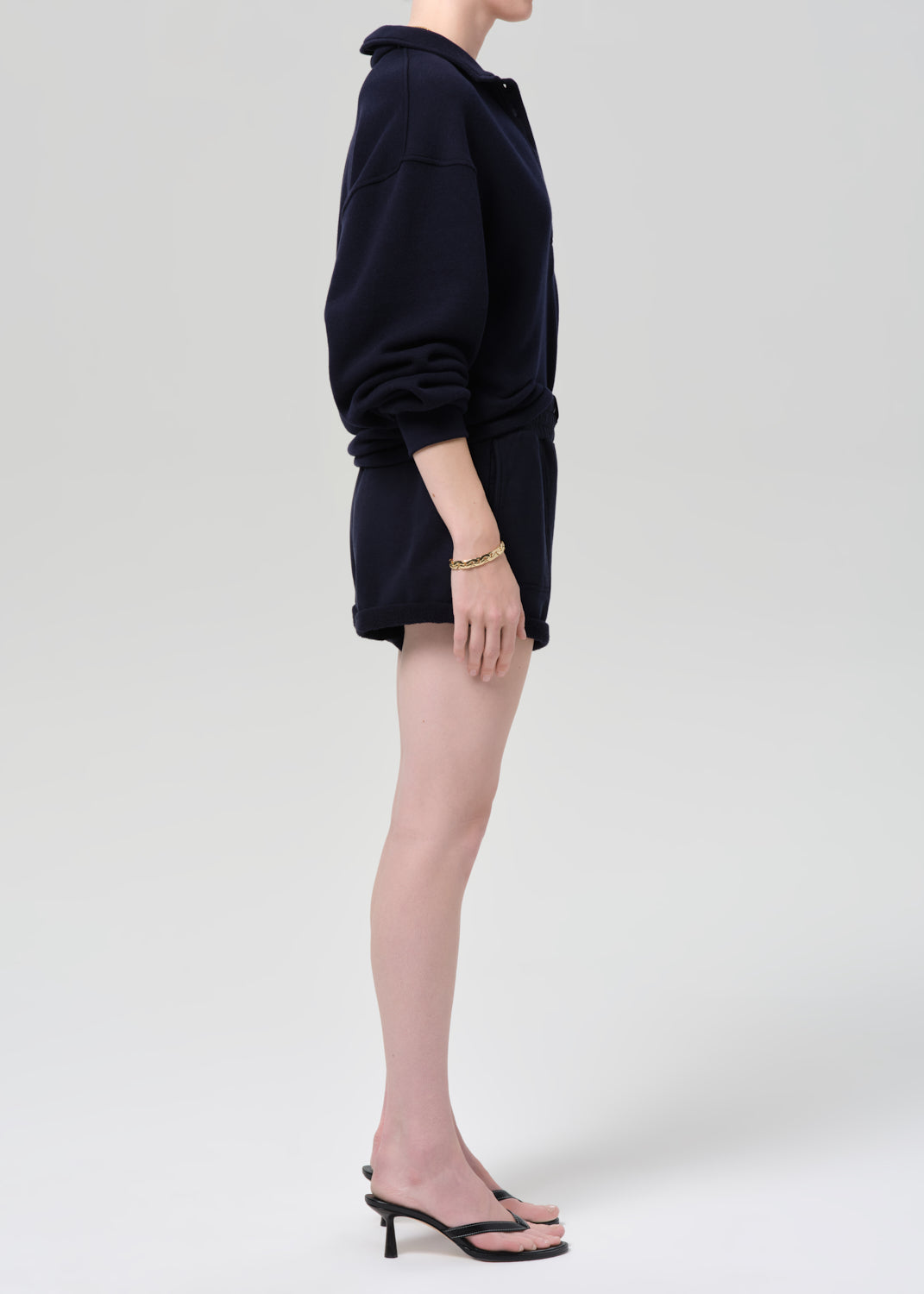 Person wearing a navy sweatshirt and shorts on a grey background