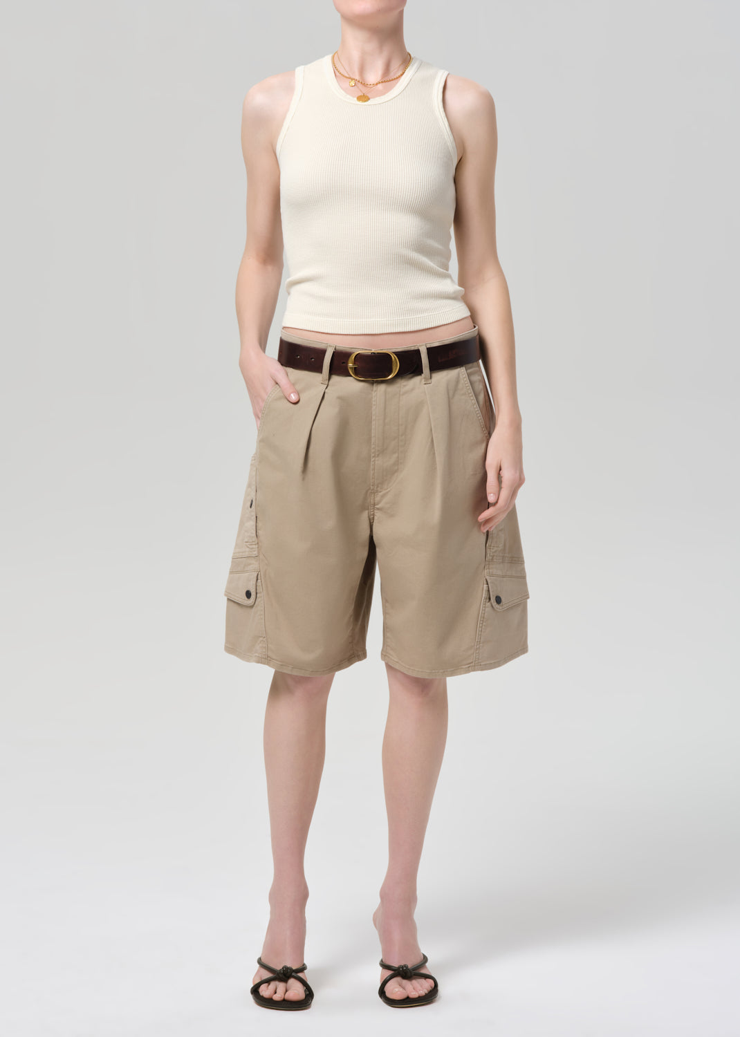 Person wearing a beige sleeveless top and beige cargo shorts on a grey background