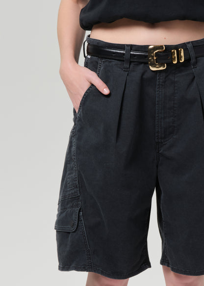 Person wearing a black top and washed black cargo shorts on a grey background