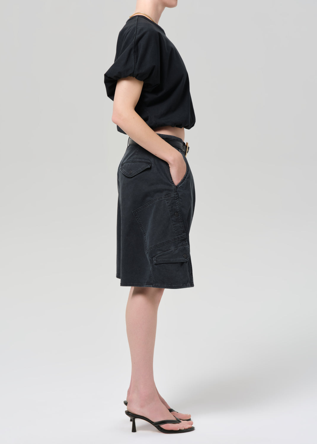 Person wearing a black top and washed black cargo shorts on a grey background