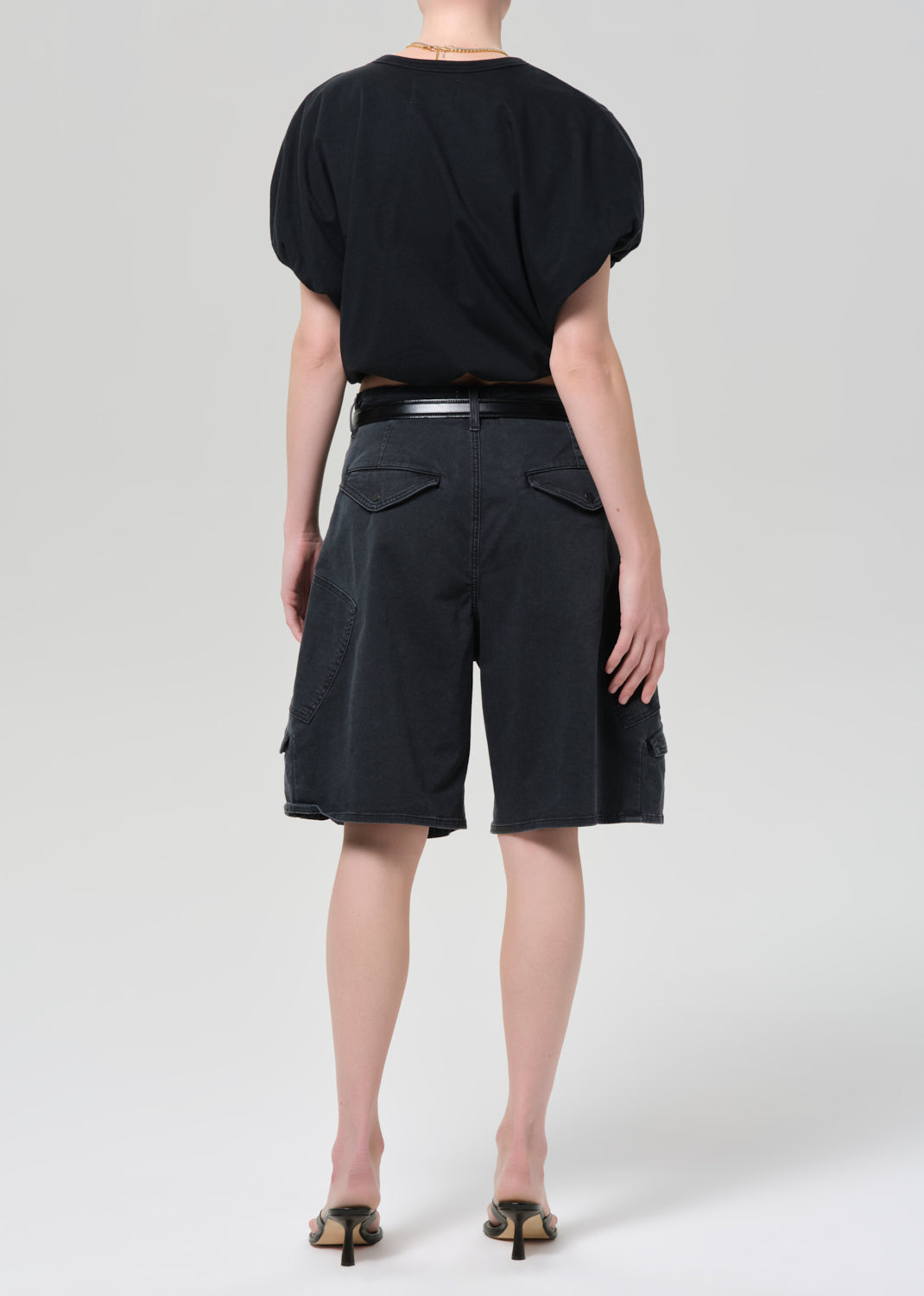 Person wearing a black top and washed black cargo shorts on a grey background