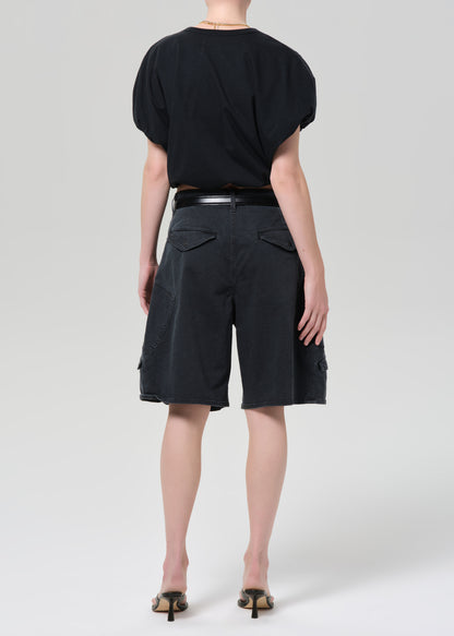 Person wearing a black top and washed black cargo shorts on a grey background