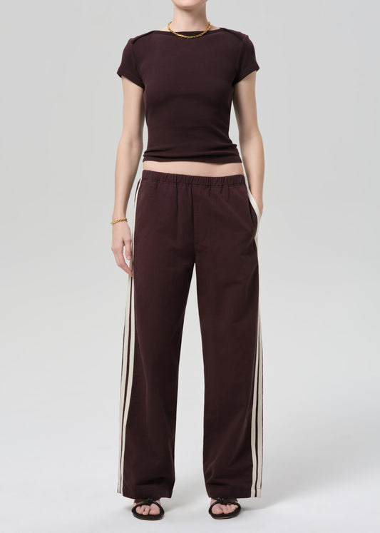 Person wearing a brown t-shirt and wide-leg pants with side stripes on a plain background
