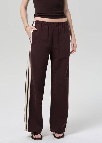 Person wearing a brown t-shirt and wide-leg pants with side stripes on a plain background
