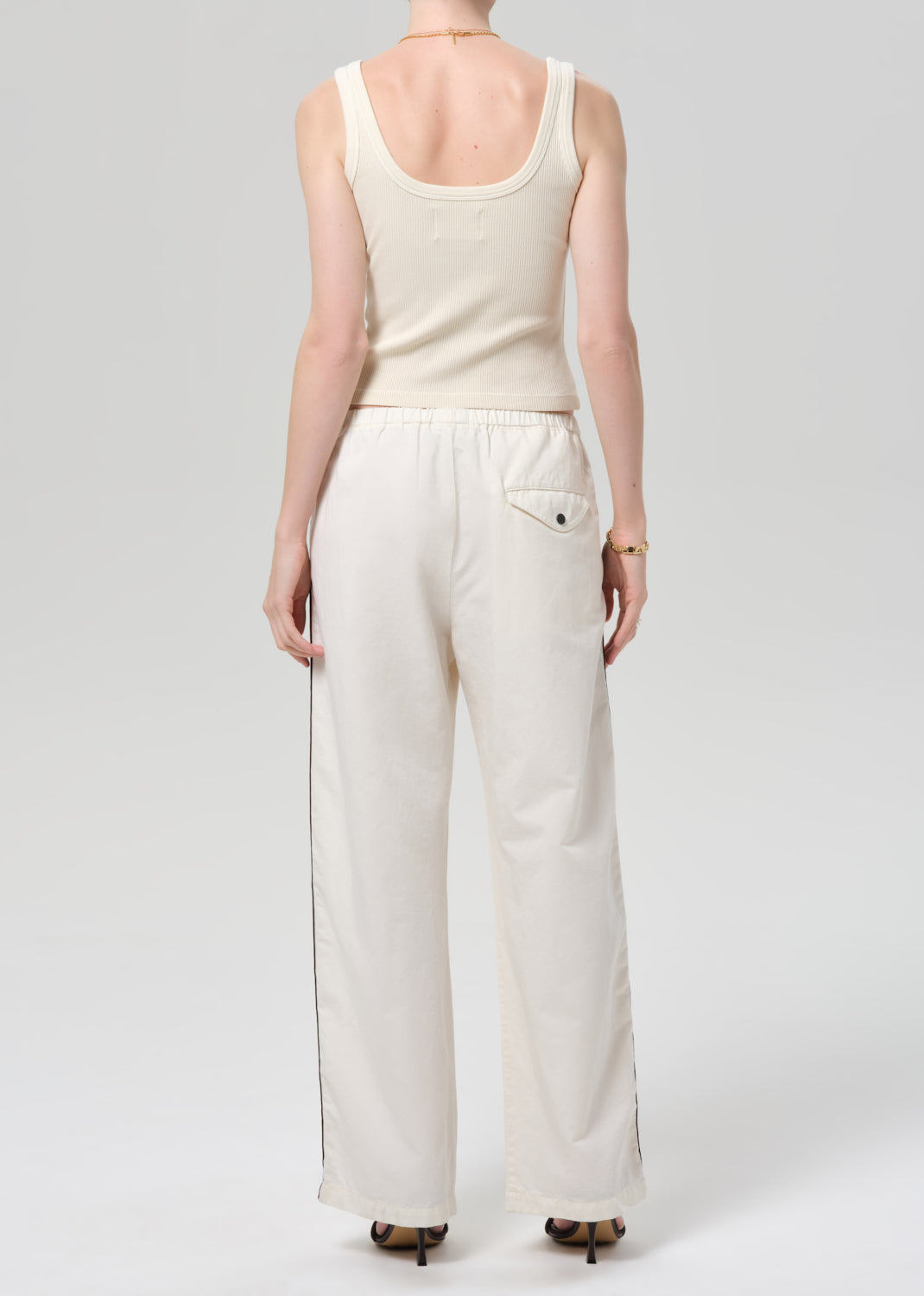 Person wearing a cream tank top and wide-leg pants with stripes on a plain background