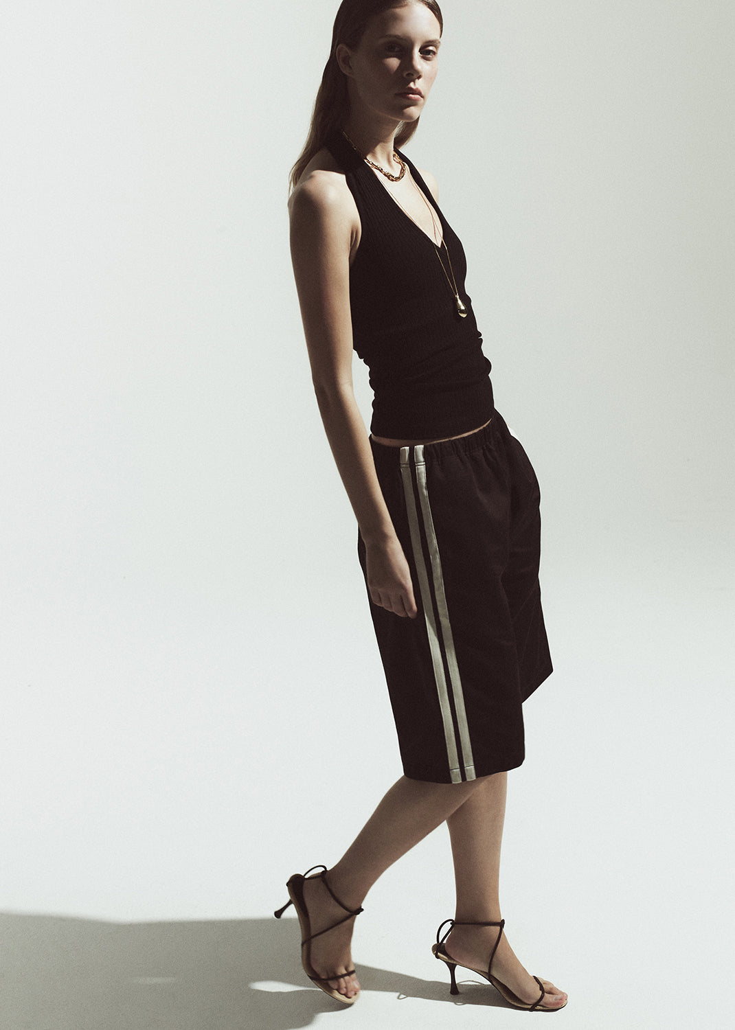 Woman wearing a brown halter top and brown shorts with white stripes on a plain background