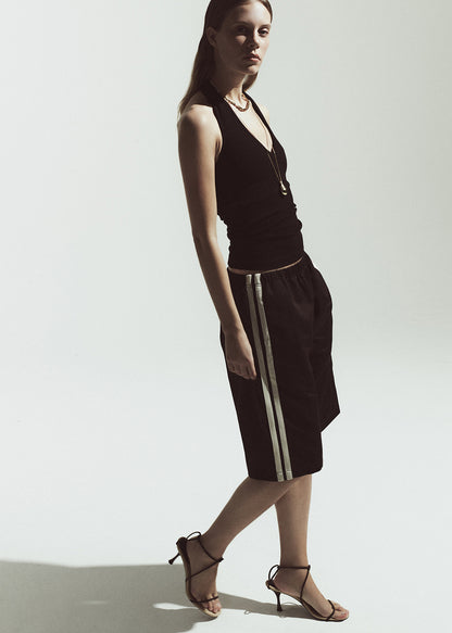 Woman wearing a brown halter top and brown shorts with white stripes on a plain background