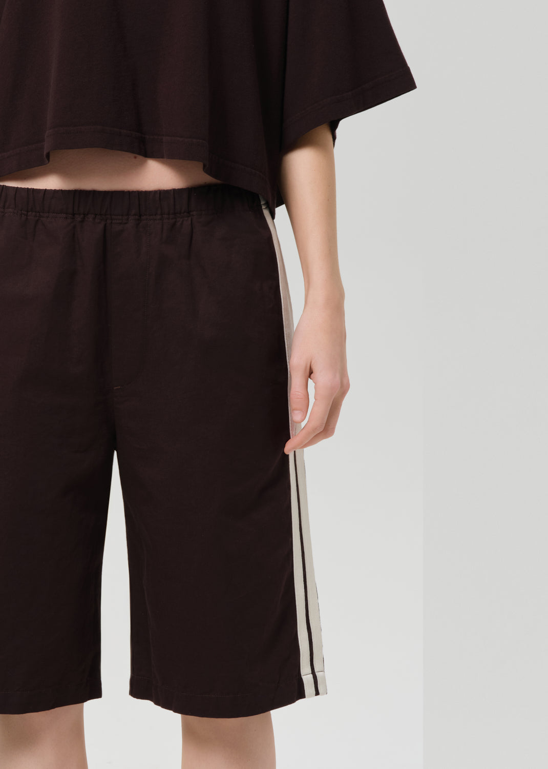 Person wearing a dark brown outfit with shorts on a plain background