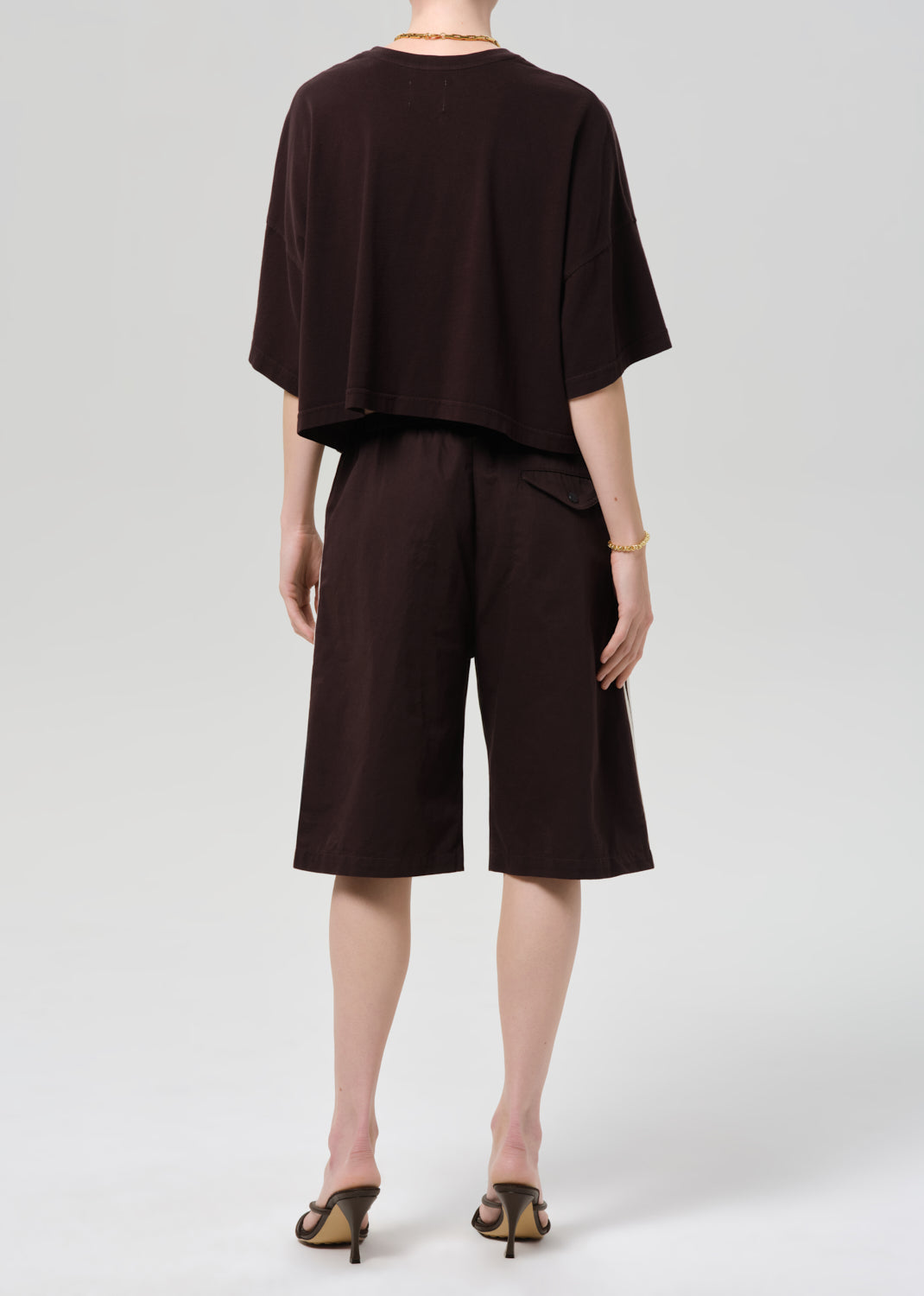 Person wearing a dark brown outfit with shorts on a plain background