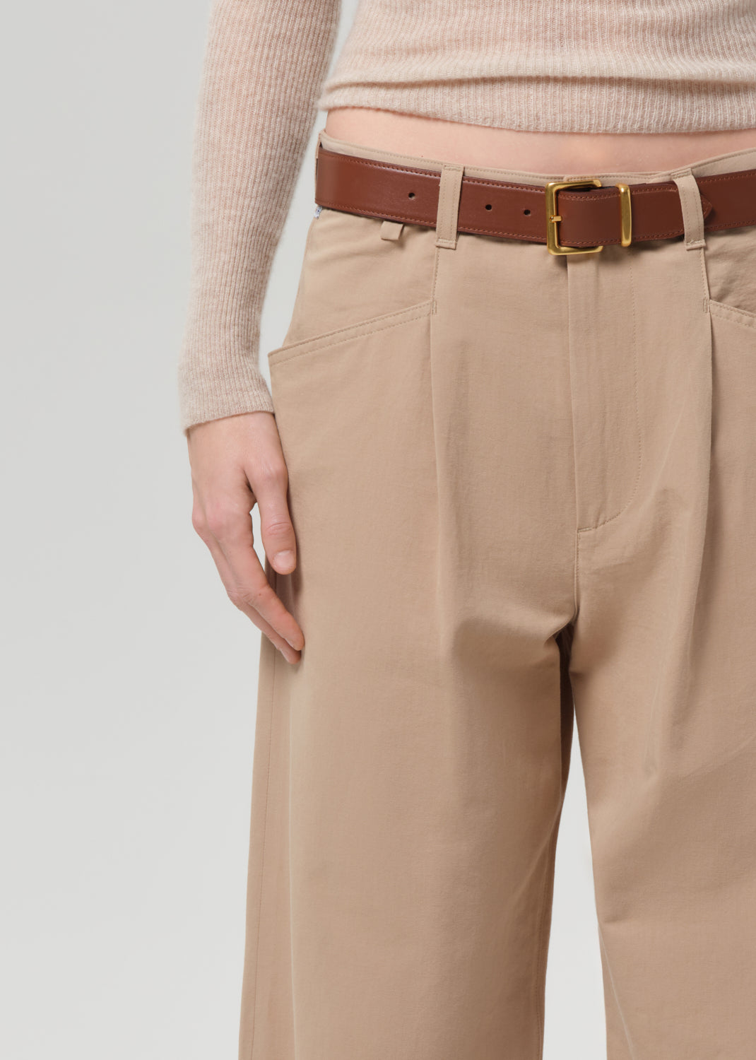 Person wearing a beige sweater and beige pants on a grey background
