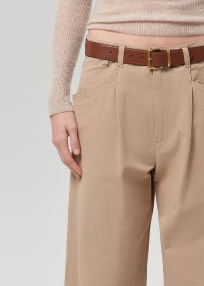 Person wearing a beige sweater and beige pants on a grey background