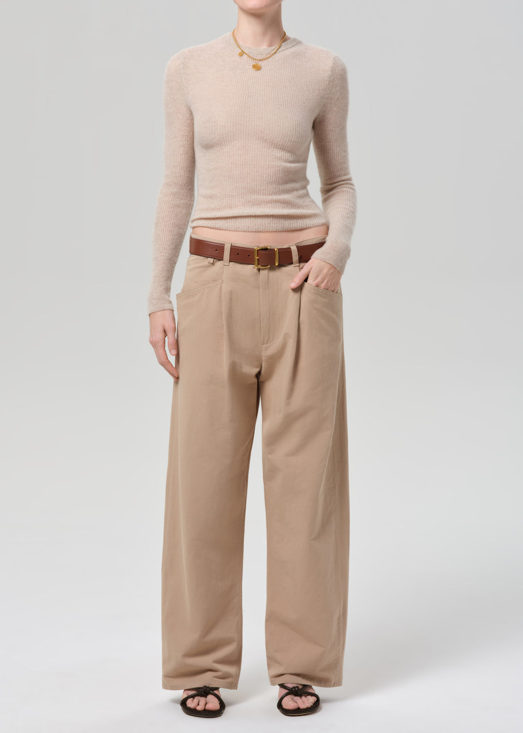 Person wearing a beige sweater and beige pants on a grey background