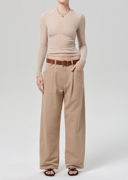 Person wearing a beige sweater and beige pants on a grey background