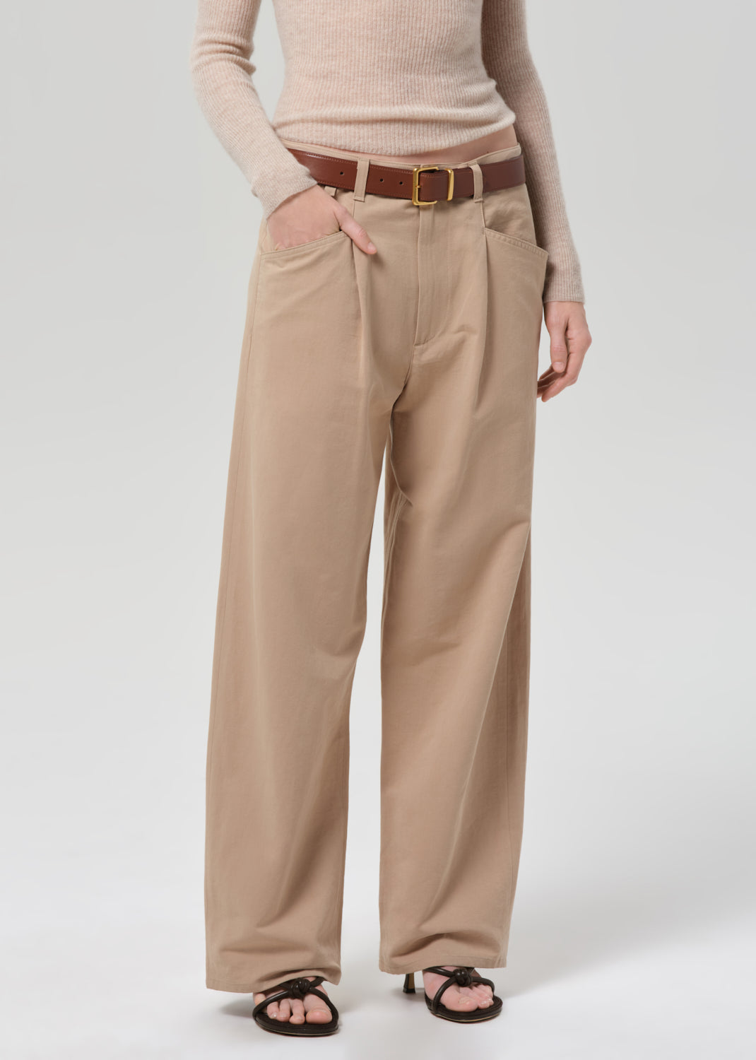Person wearing a beige sweater and beige pants on a grey background