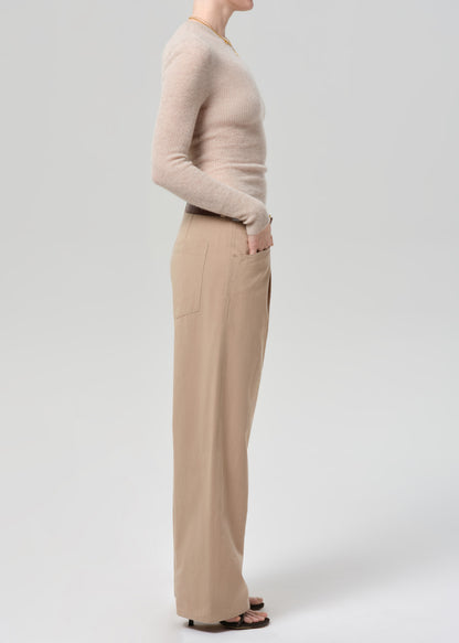 Person wearing a beige sweater and beige pants on a grey background