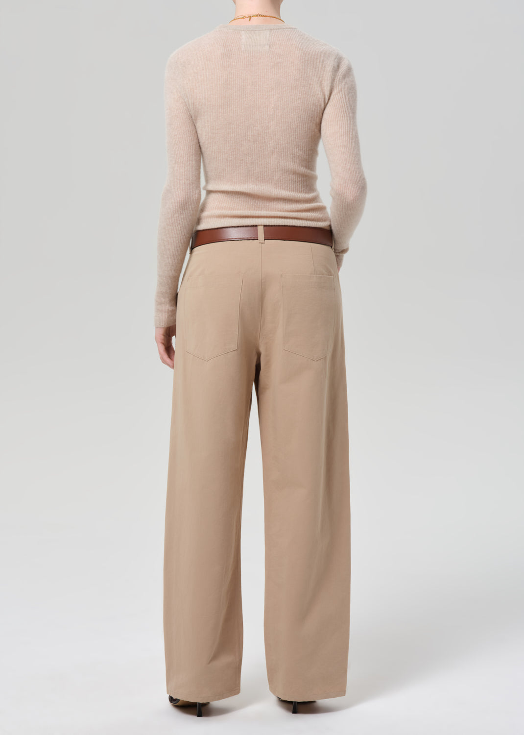 Person wearing a beige sweater and beige pants on a grey background