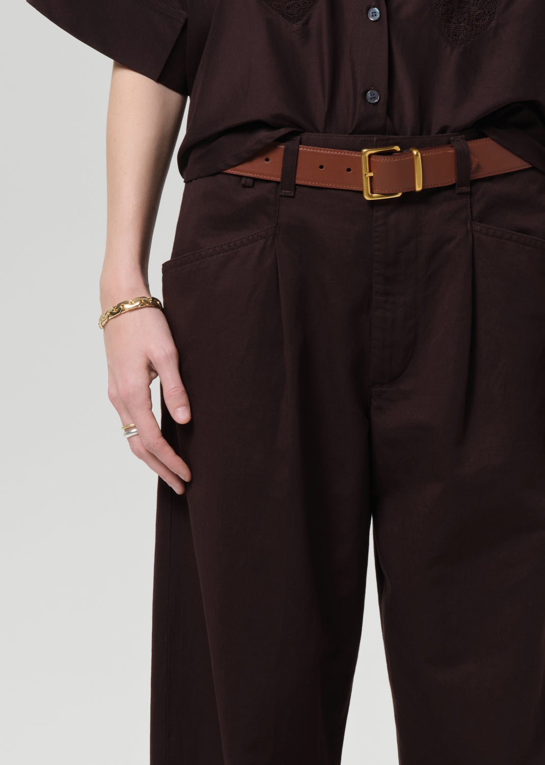 Person wearing a brown shirt and wide-leg pants on a grey background