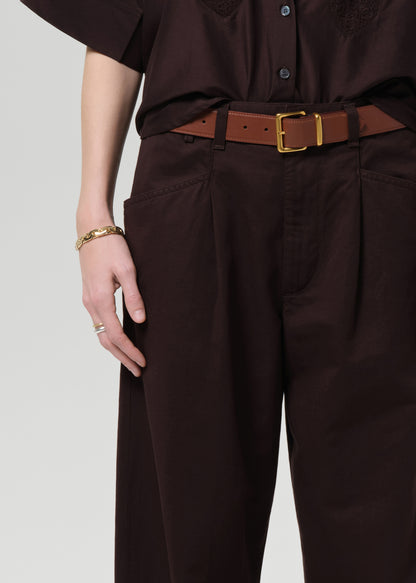 Person wearing a brown shirt and wide-leg pants on a grey background
