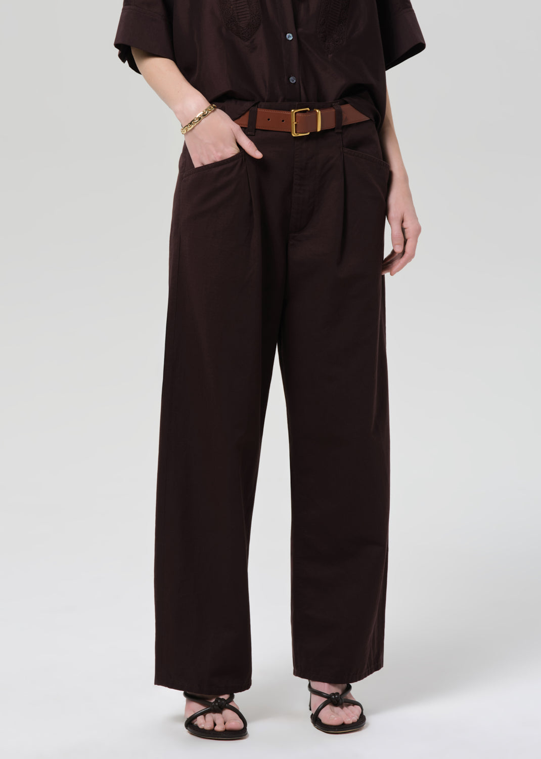 Person wearing a brown shirt and wide-leg pants on a grey background