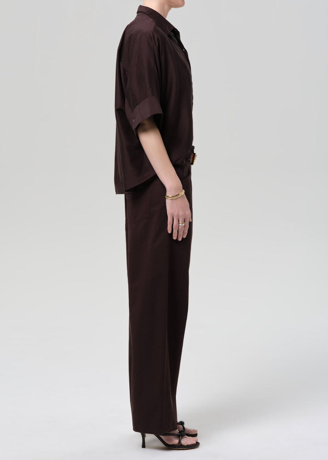 Person wearing a brown shirt and wide-leg pants on a grey background