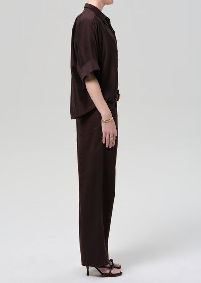 Person wearing a brown shirt and wide-leg pants on a grey background