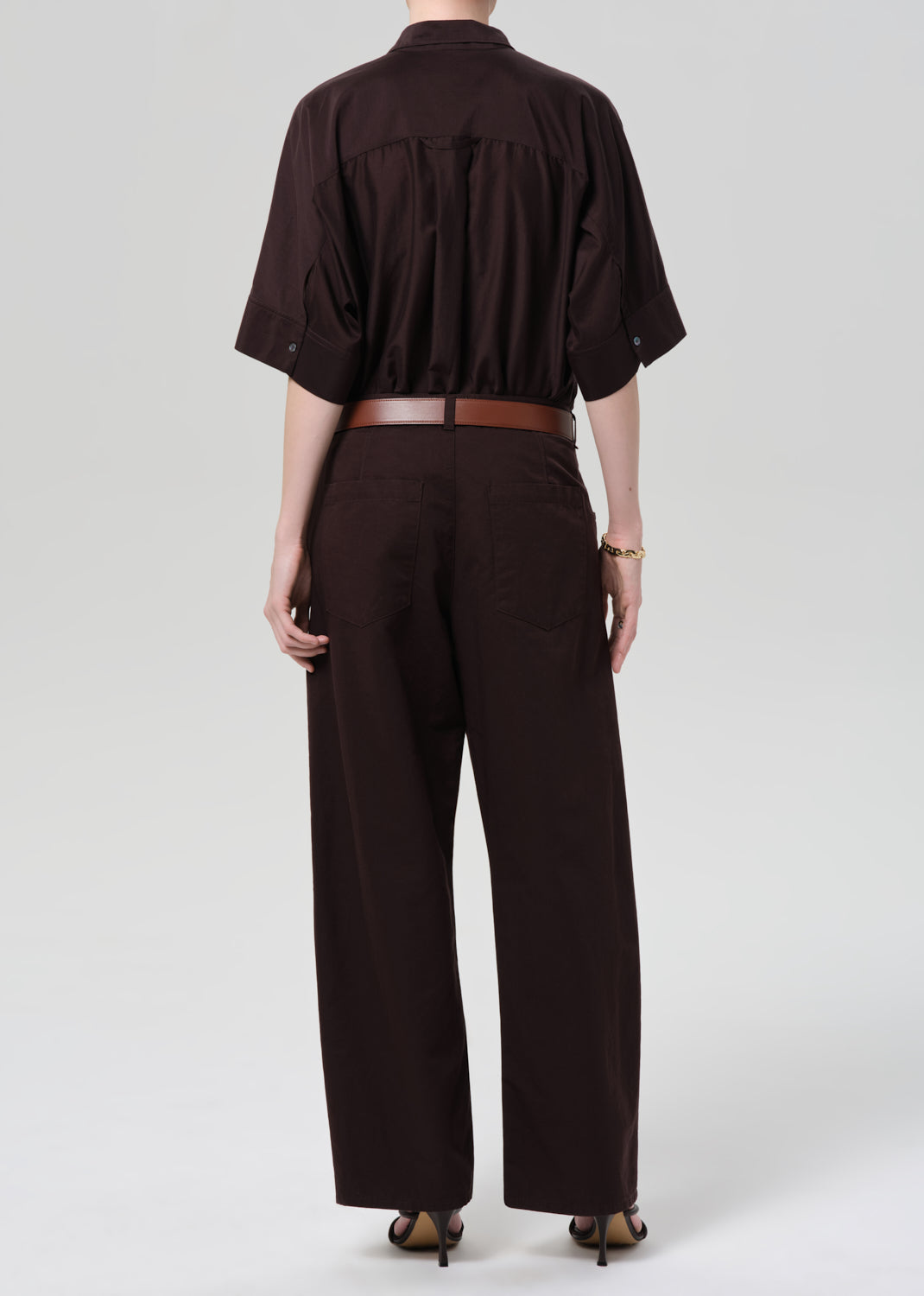 Person wearing a brown shirt and wide-leg pants on a grey background
