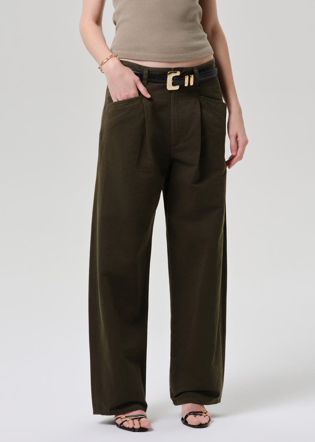 Person wearing brown wide-leg pants with a belt on a grey background