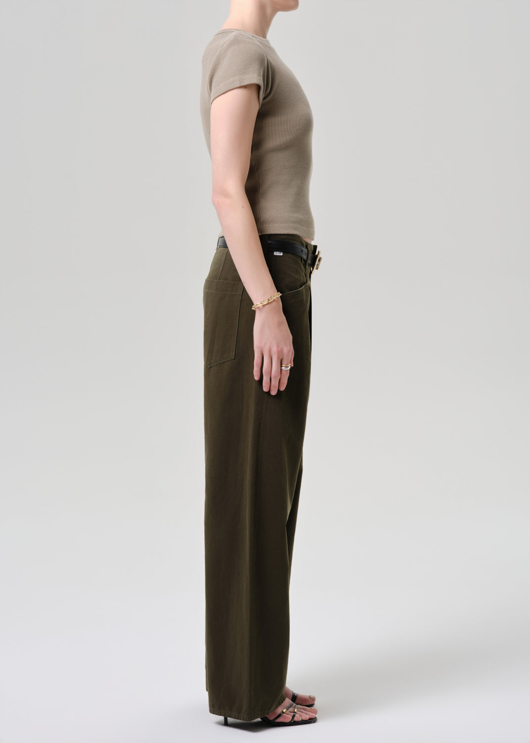 Person wearing a beige top and dark green pants on a grey background