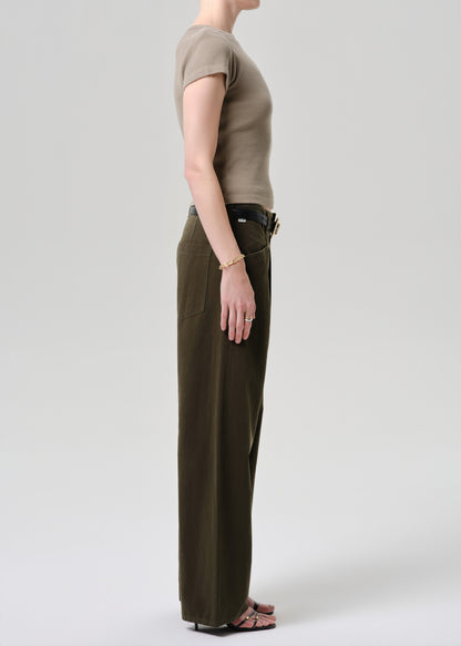 Person wearing a beige top and dark green pants on a grey background