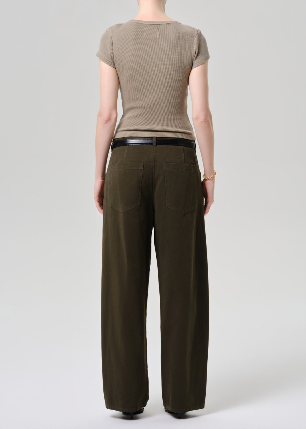 Person wearing a brown t-shirt and dark brown pants on a grey background