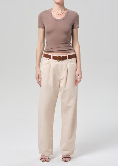 Person wearing a brown top and pale peach pants on a grey background