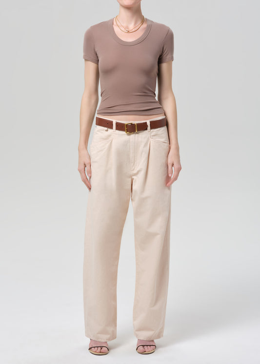 Person wearing a brown top and pale peach pants on a grey background