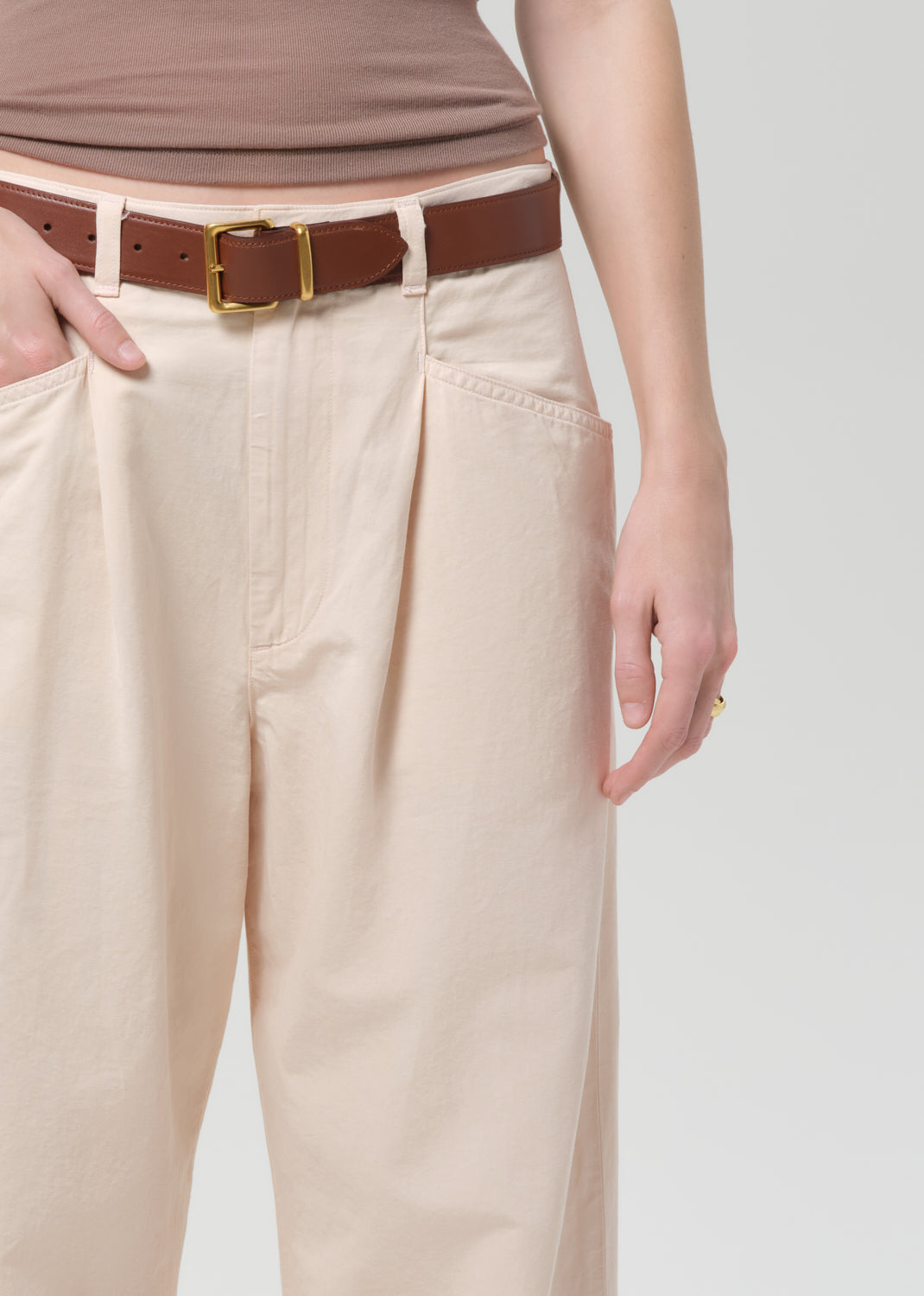 Person wearing a brown top and pale peach pants on a grey background