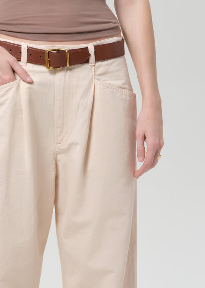 Person wearing a brown top and pale peach pants on a grey background