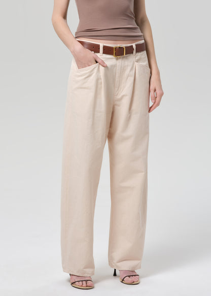 Person wearing a brown top and pale peach pants on a grey background