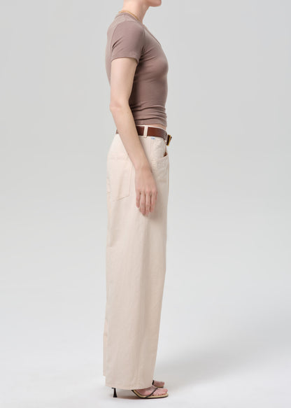 Person wearing a brown top and pale peach pants on a grey background