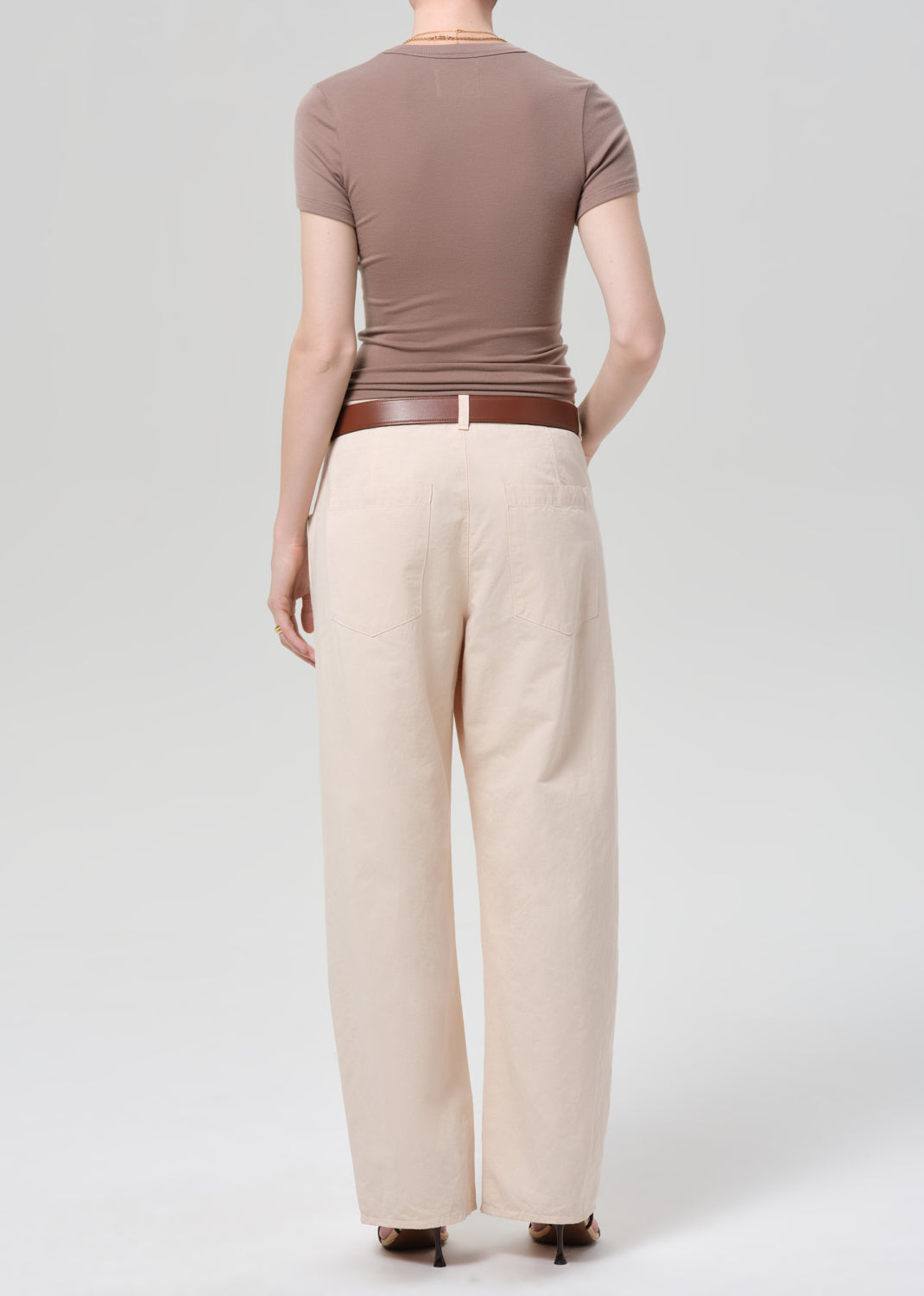Person wearing a brown top and pale peach pants on a grey background