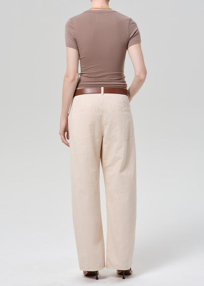 Person wearing a brown top and pale peach pants on a grey background