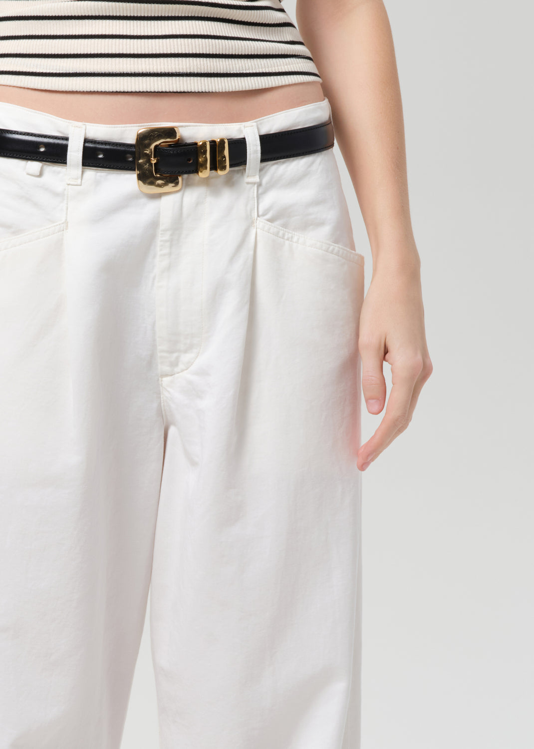 Person wearing a black and white striped top with white pants and a black belt on a plain background