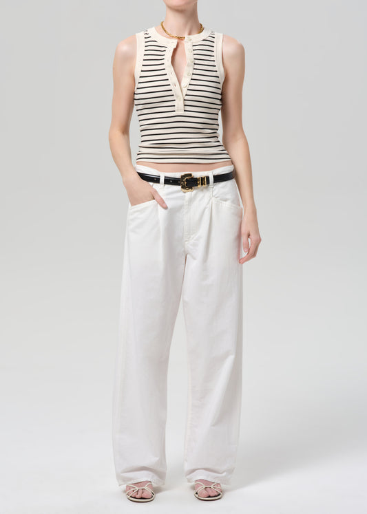 Person wearing a striped sleeveless top and white pants on a plain background