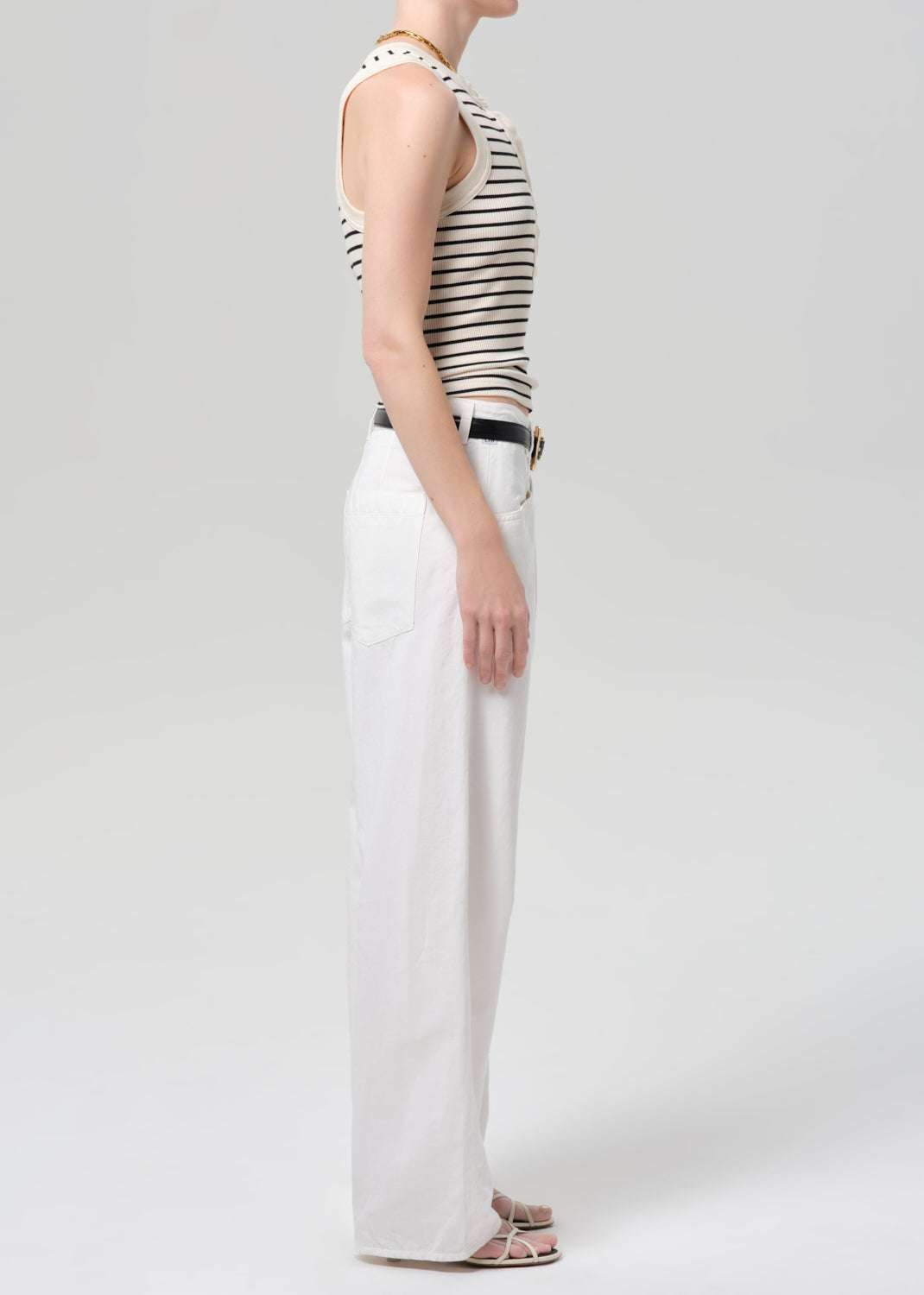 Person wearing a striped tank top and white pants on a plain background