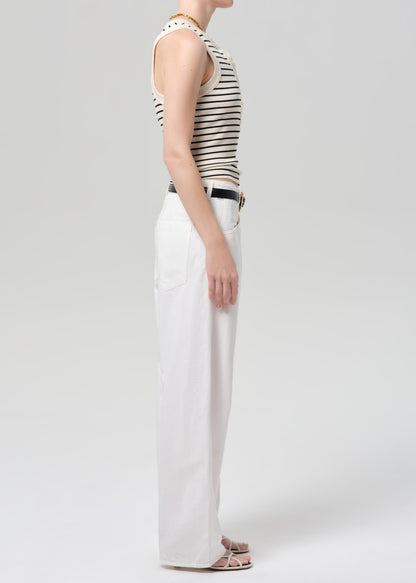 Person wearing a striped tank top and white pants on a plain background