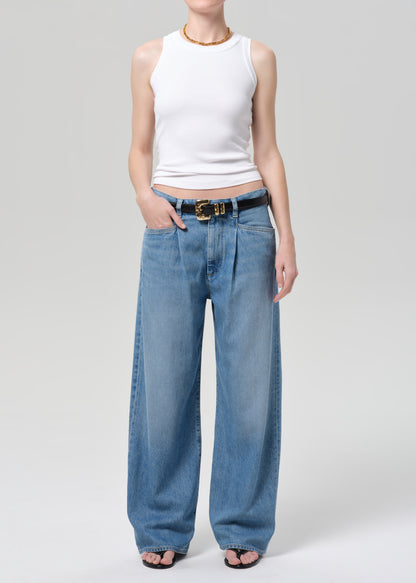 Person wearing a white sleeveless top and blue jeans on a plain background