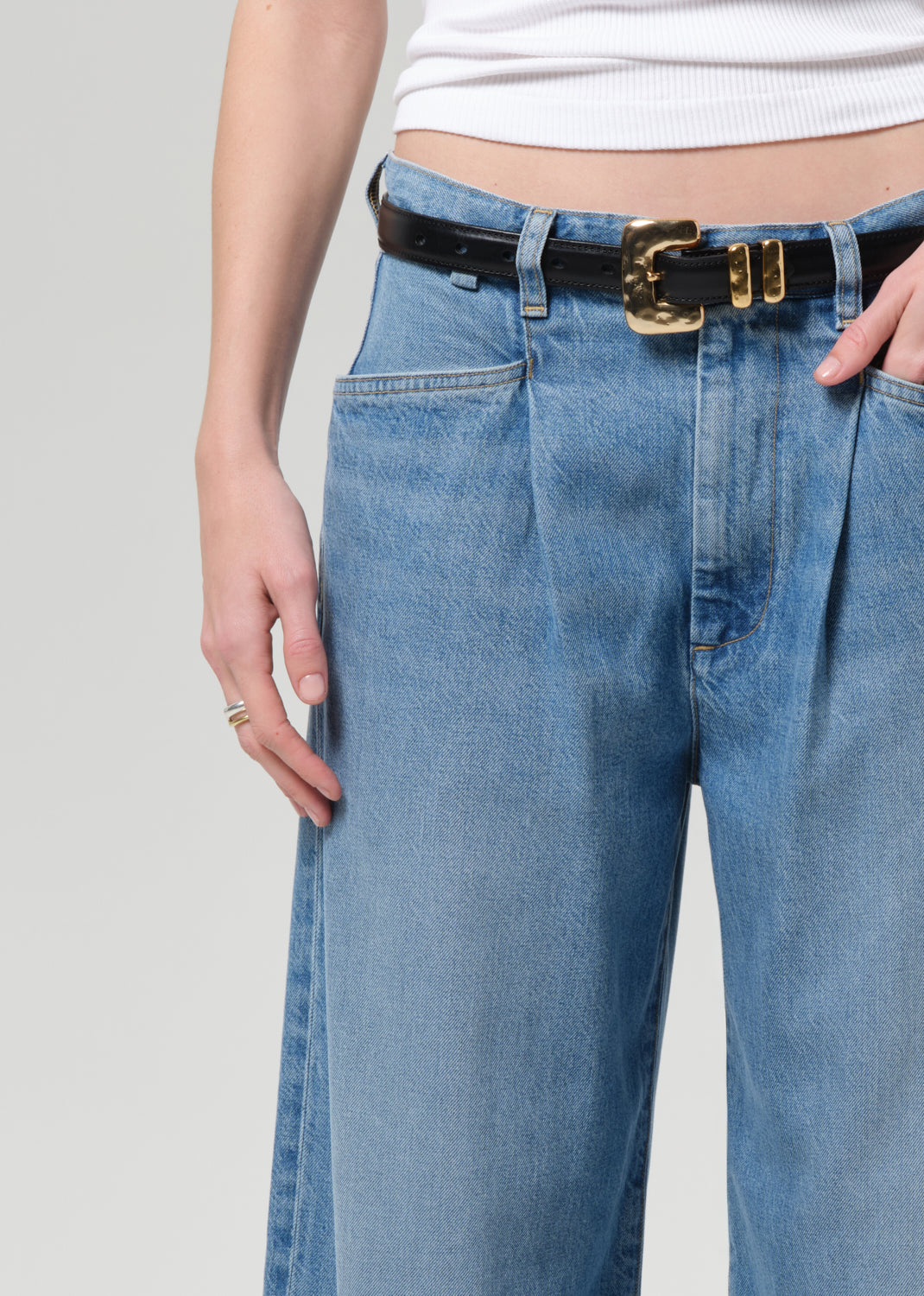 Person wearing blue jeans with a black belt on a plain background