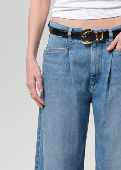 Person wearing blue jeans with a black belt on a plain background