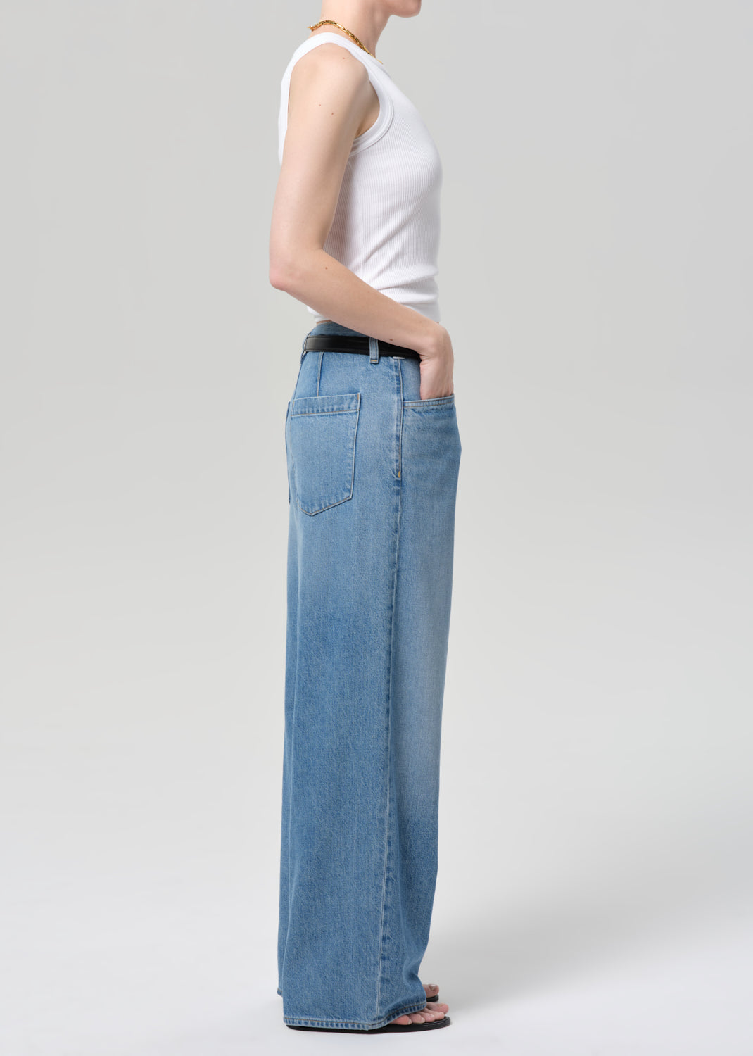 Person wearing a white sleeveless top and blue jeans on a light gray background