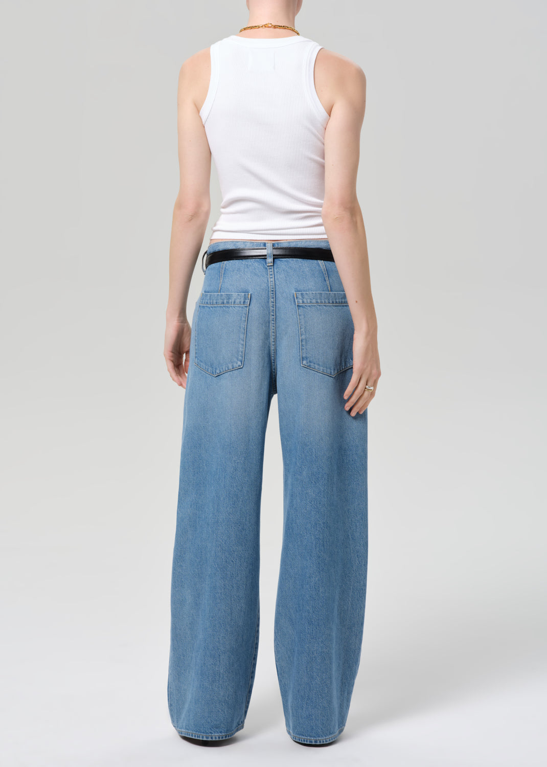 Person wearing light blue jeans and a white sleeveless top on a plain background