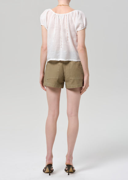 Person wearing a white blouse and beige shorts on a plain background