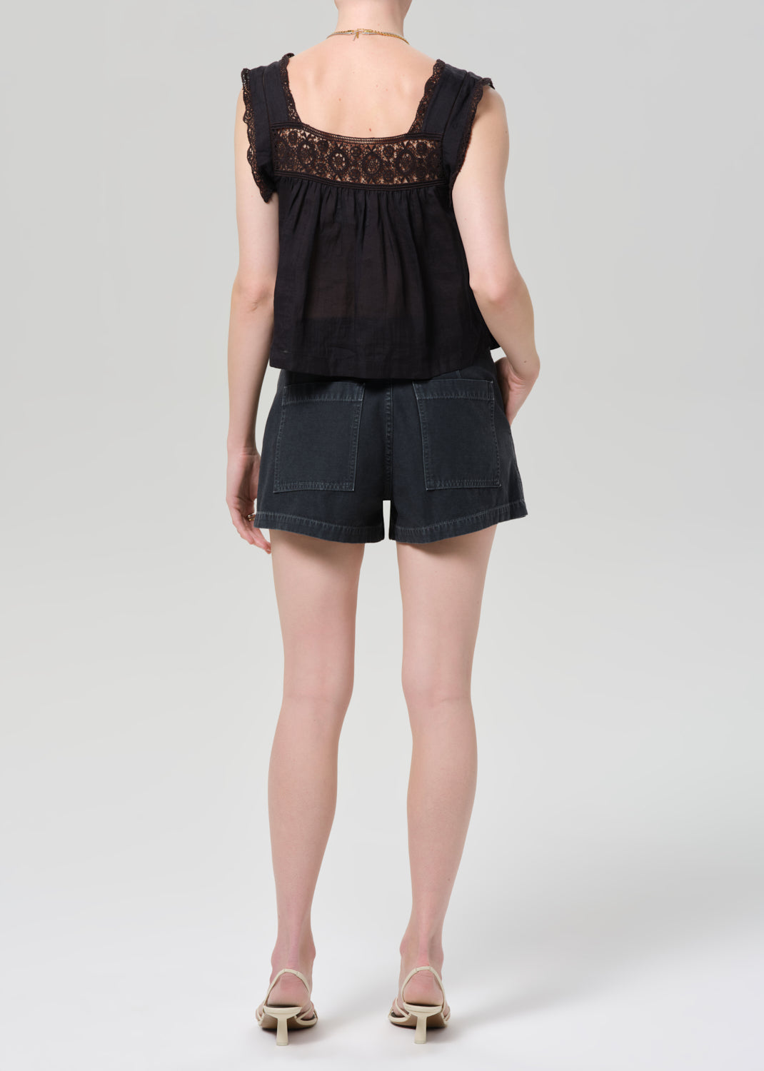Person wearing a black sleeveless top with lace details and black shorts on a grey background